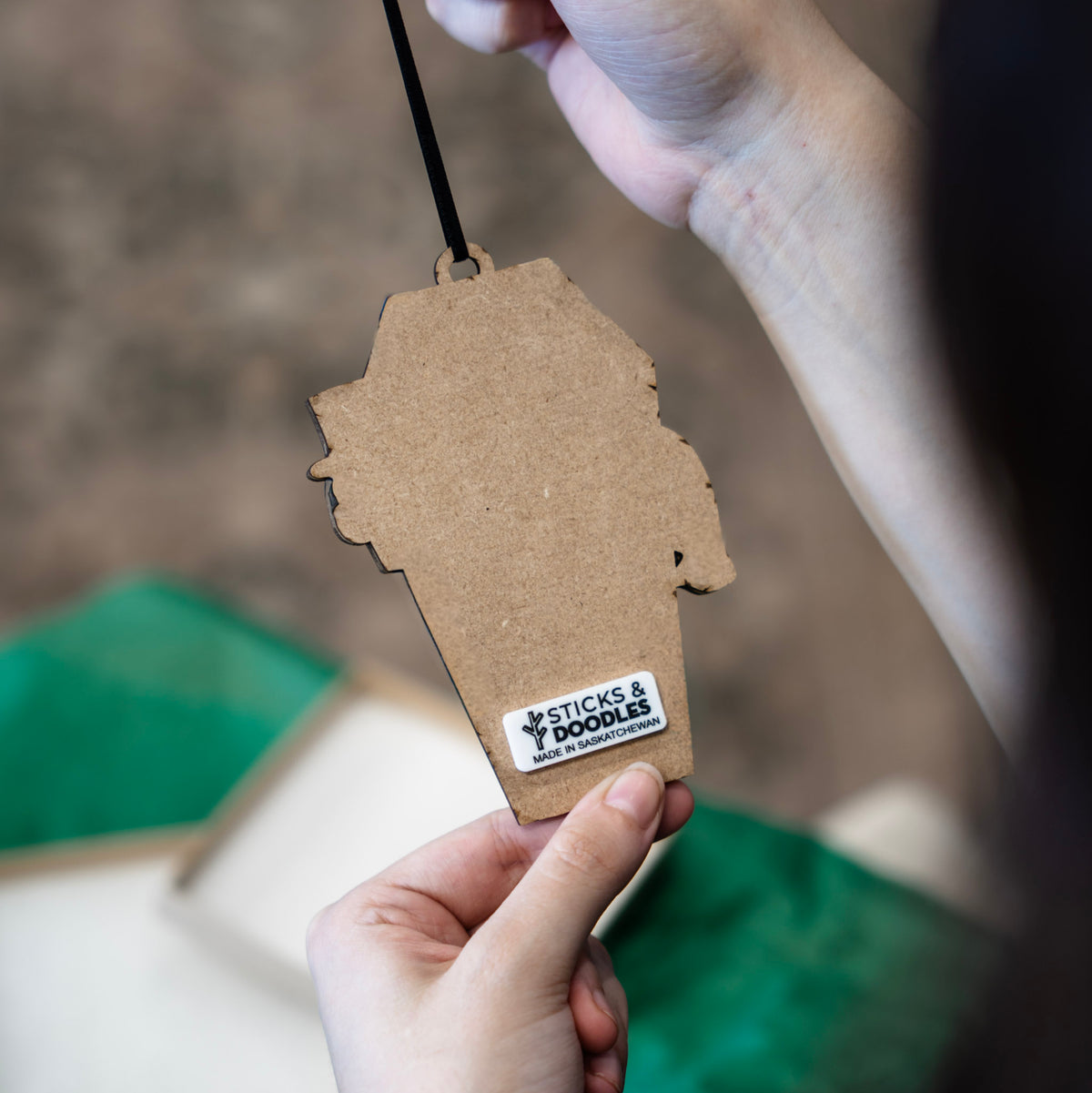 A person holds the back of a coffin-shaped wooden ornament, against a blurred background.
