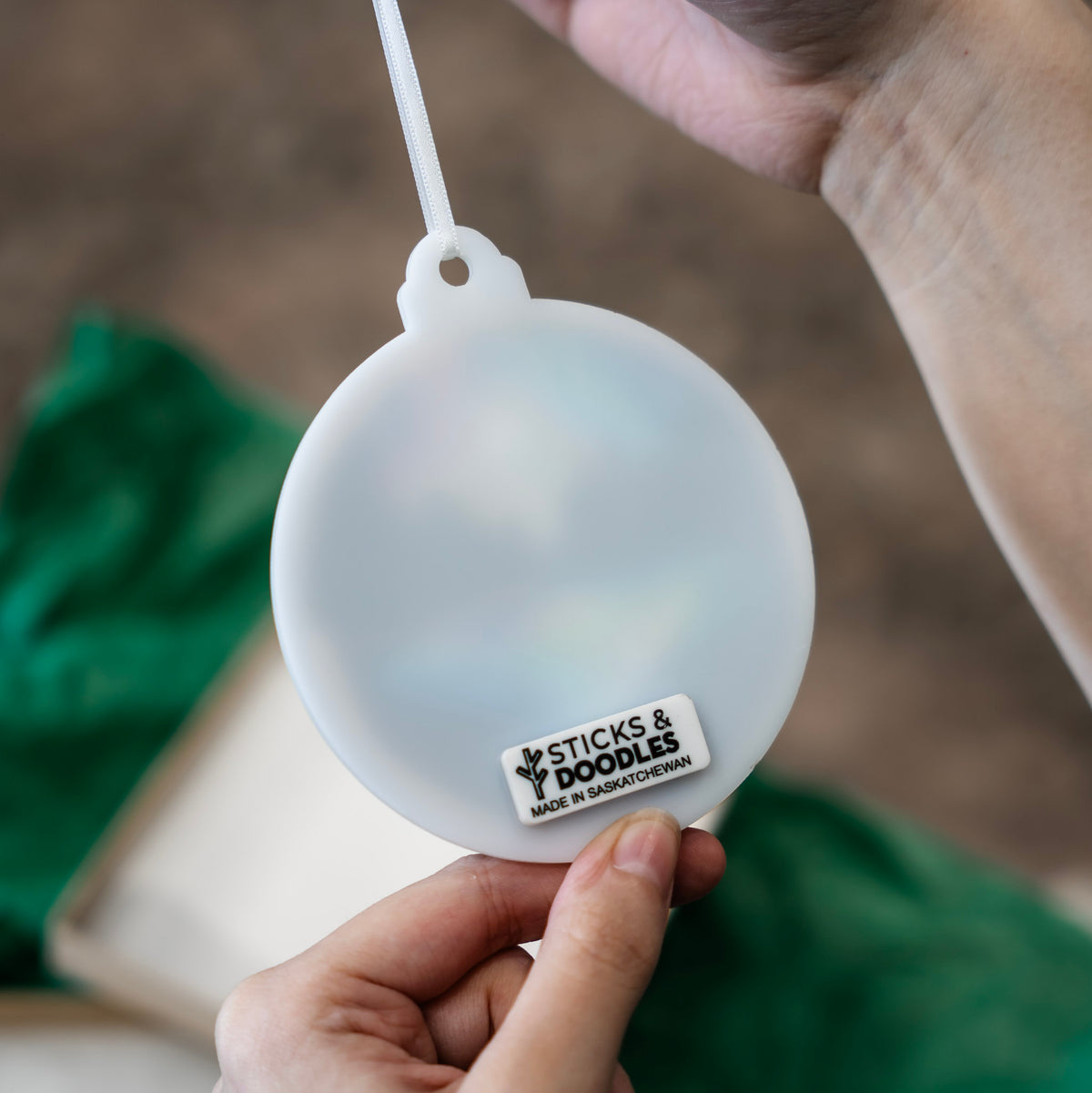 Back of the round white acrylic ornament with the tag Sticks & Doodles Made in Saskatchewan.