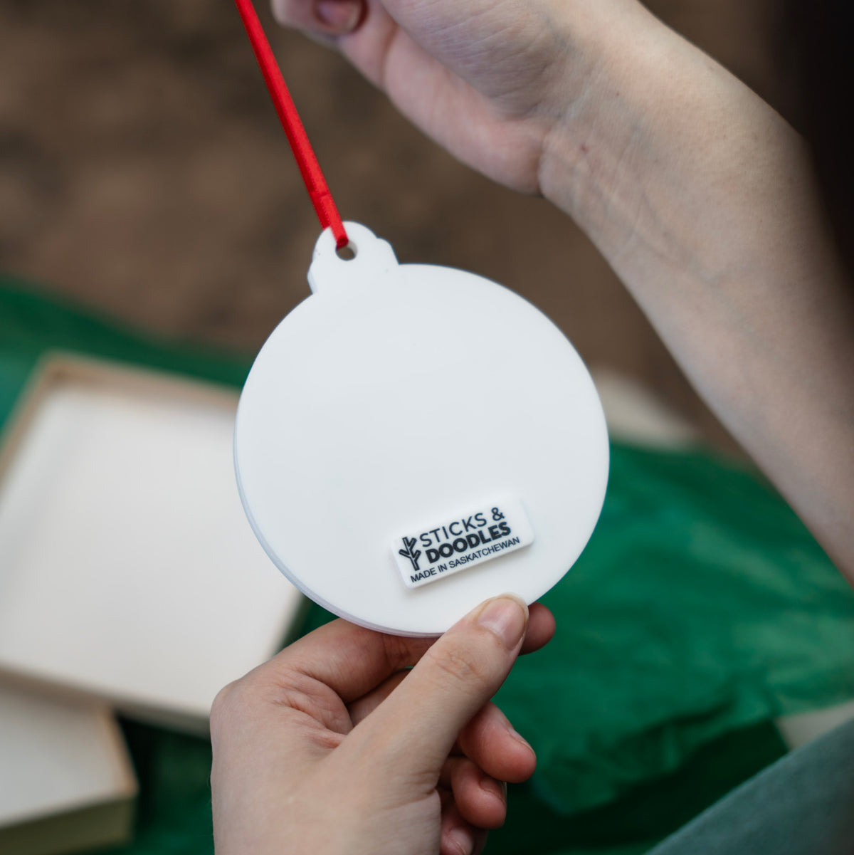 A person holds the backside of the Pooh ornament to show off the ornament ribbon and Sticks & Doodles tag.