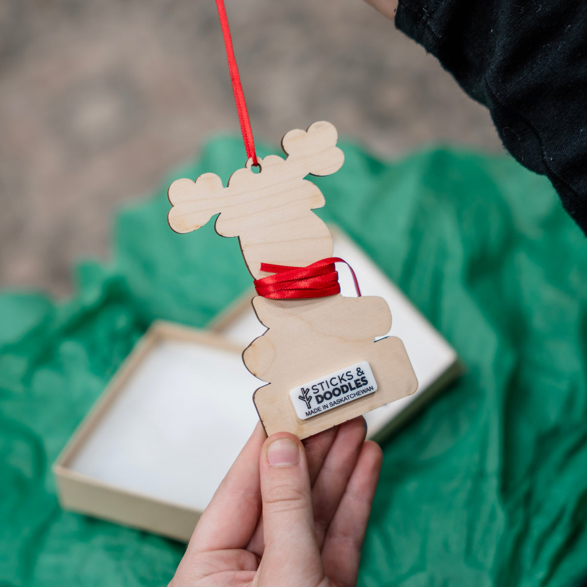 The back of the rudolph wood ornament with a tag that says STICKS & DOODLES MADE IN SASKATCHEWAN.