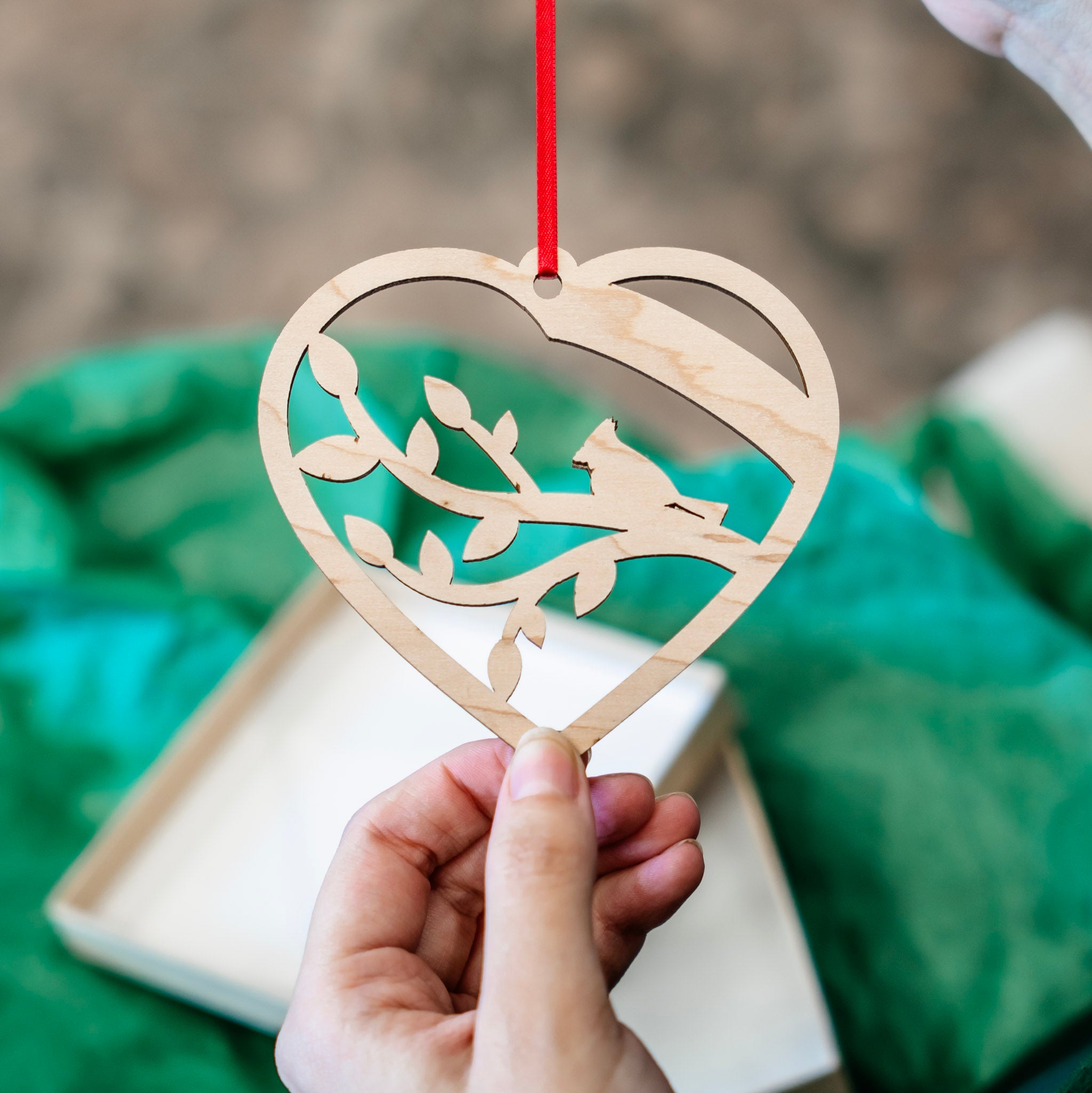 The back of a heart-shaped wooden ornament with an outline of a branch with a bird on top.