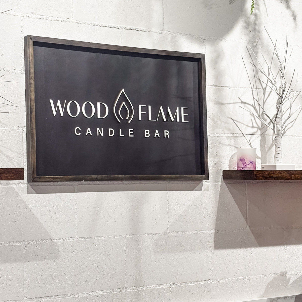 Framed Wood and Flame Candle Bar business sign installed on a white brick wall