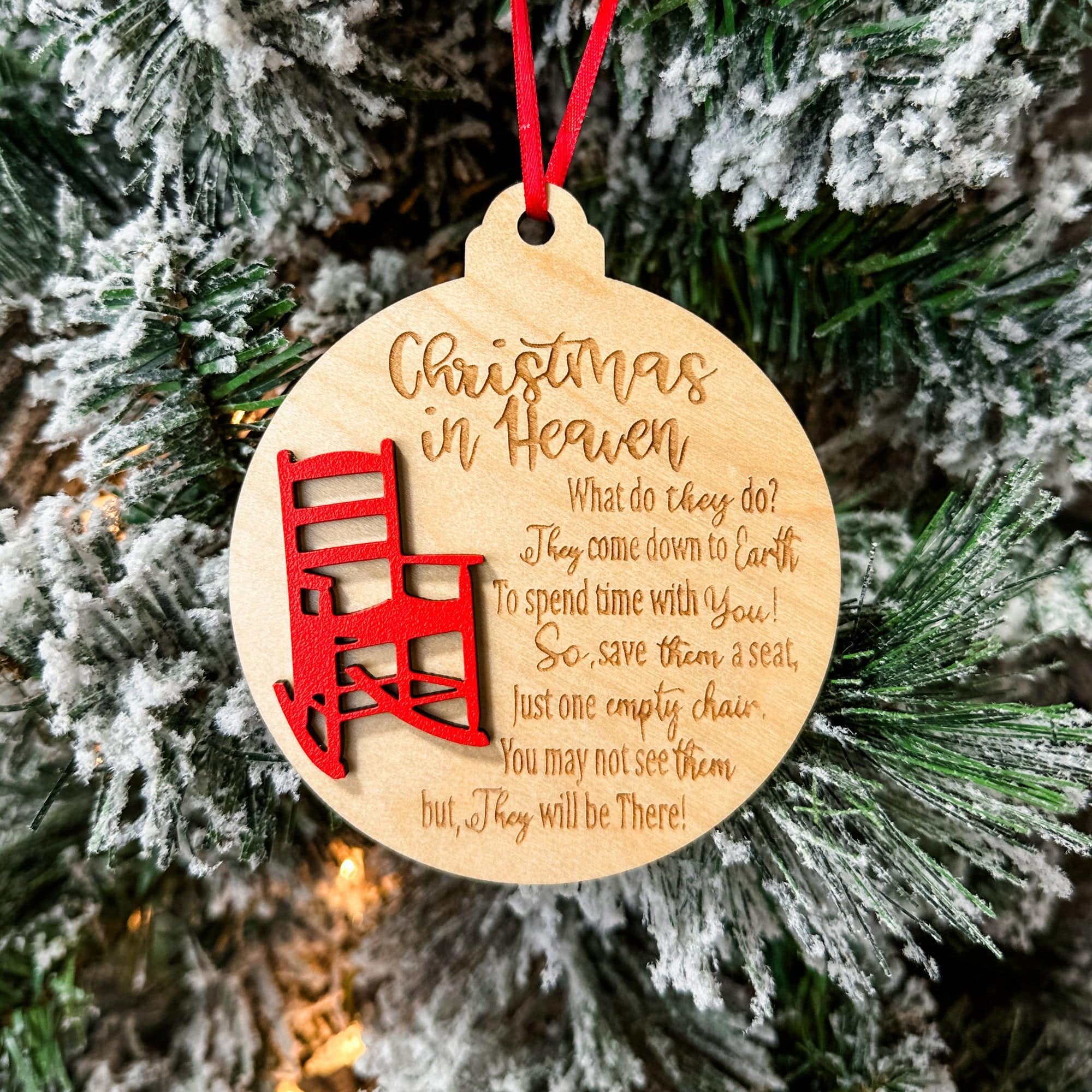 A wooden Christmas ornament with a red rocking chair design and the text 'Christmas in Heaven' engraved on it, displayed against a Christmas tree background.