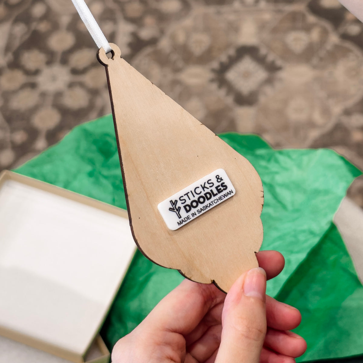 Back of gnome ornament made out of wood and has a white tag that says STICKS & DOODLES MADE IN SASKATCHEWAN.